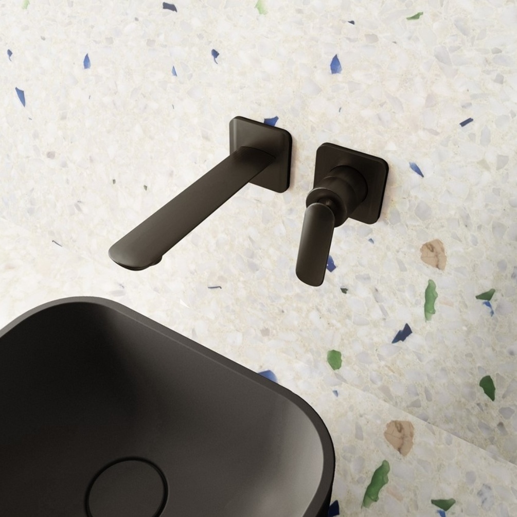 Lifestyle image of the Crosswater Huck Matt Black Wall Mounted Basin Mixer installed on a white terrazzo wall, above a black countertop basin